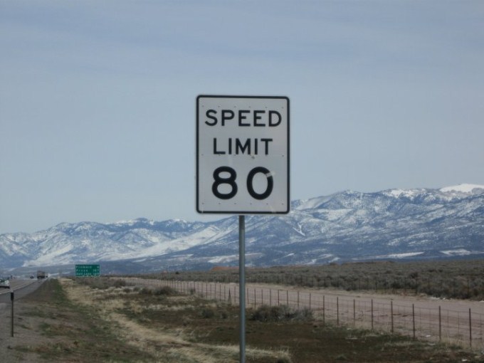 This photo shows the number 80 on a speed limit sign next to the open road.